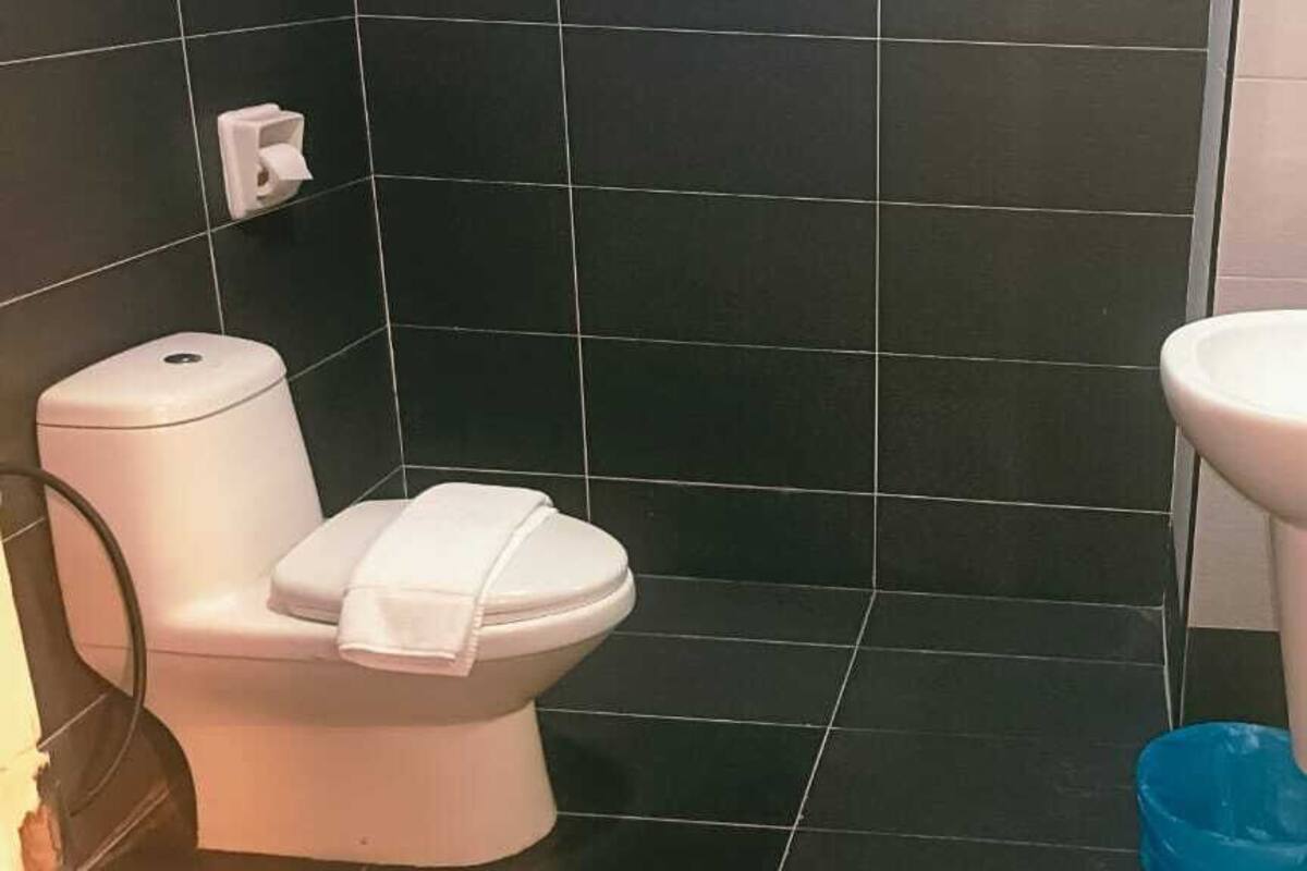 A bathroom with a toilet and sink, black tiled walls, and a blue trash bin.