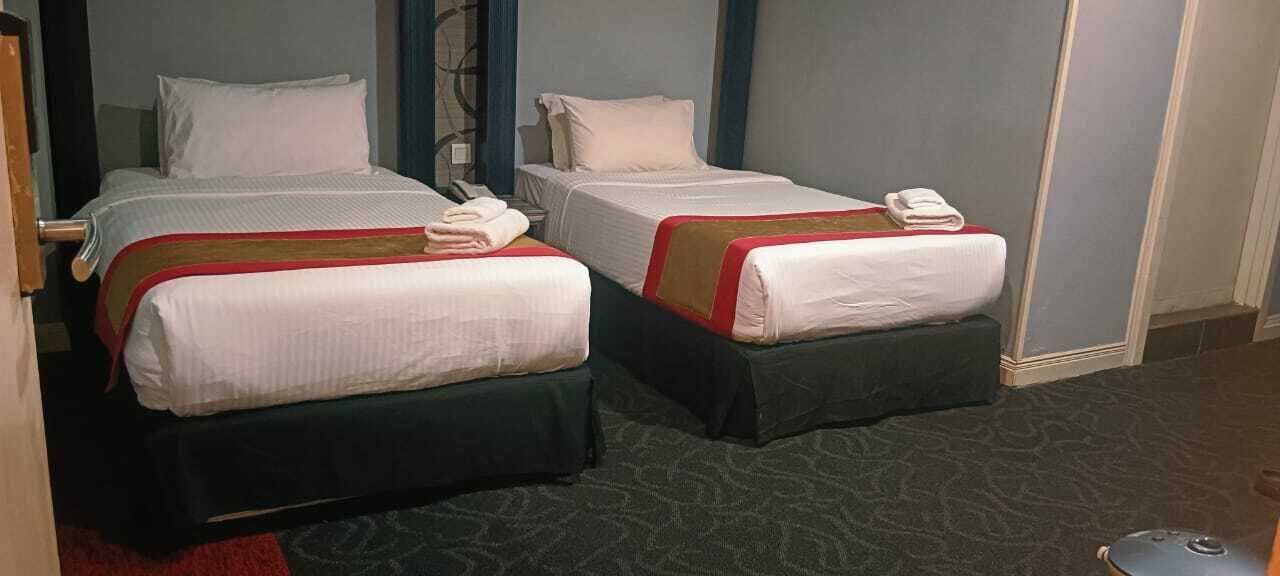 Two single beds with white linens and red accents, a telephone on the left bed, and a red carpeted floor.