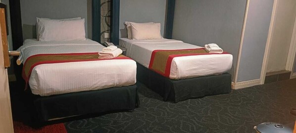 Deux lits simples avec du linge de lit blanc et des touches de rouge, un téléphone sur le lit de gauche et un sol recouvert d’une moquette rouge.
