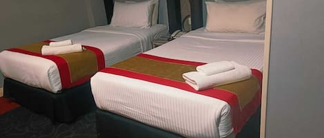 Two neatly made beds with white linens and red accents, a telephone on the nightstand, and a dark carpeted floor.