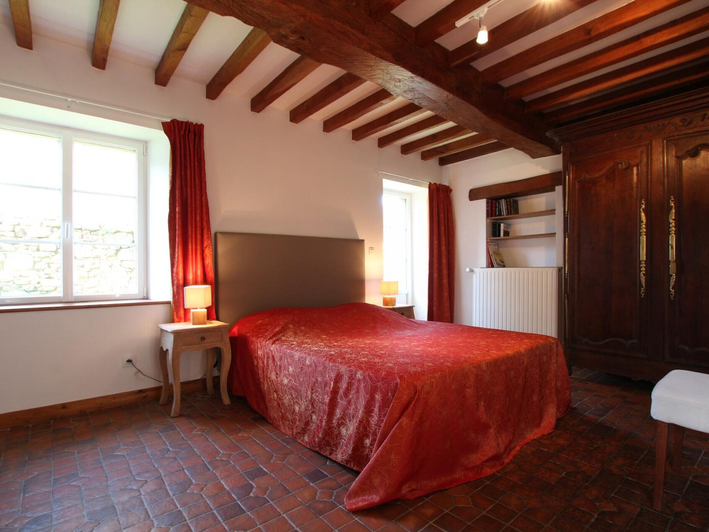 A bedroom with a large bed, wooden beams, a radiator, and a window with curtains.
