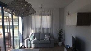 Ein modernes Wohnzimmer mit grauem Sofa, einem großen Fenster, einem Topf mit Pflanze und einem Flachbildfernseher.