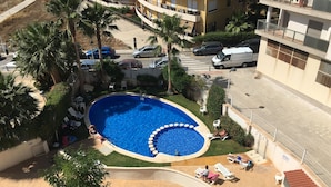 Ein Swimmingpool mit einer runden Lounge-Area, umgeben von Palmen und einer Terrasse mit Liegestühlen und Tischen.