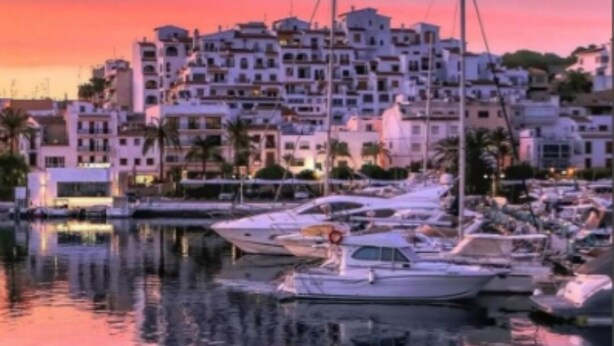 Ein Yachthafen mit vertäuten Booten, ein Gebäude am Wasser und ein Sonnenuntergangshimmel.