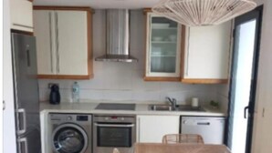 Eine moderne Küche mit Edelstahlgeräten, einem Backofen, einer Waschmaschine und einem Essbereich mit Holztisch und Stühlen.