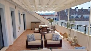 Eine Dachterrasse mit einer Sofagruppe, einem Esstisch mit Stühlen und einer Statue.
