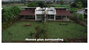 A modern two-story house with a central staircase, surrounded by a well-maintained lawn and greenery. - The Quade Villa By Spandan Holiday Homes (Anjaneri)