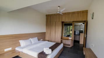 Ein Schlafzimmer mit Bett, Holz-Kopfteil, Deckenventilator, einer Küchenzeile und einem durch eine offene Tür einsehbaren Badezimmer.