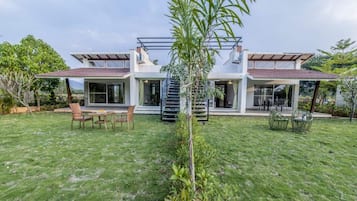 A modern house with a large backyard, a small tree, and outdoor furniture.