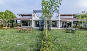 Une maison moderne avec un grand jardin, un petit arbre et du mobilier d’extérieur.