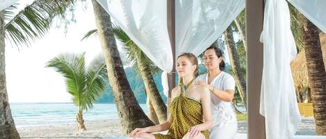 Un couple sur une plage, sous un auvent, avec une table de massage et une serviette.