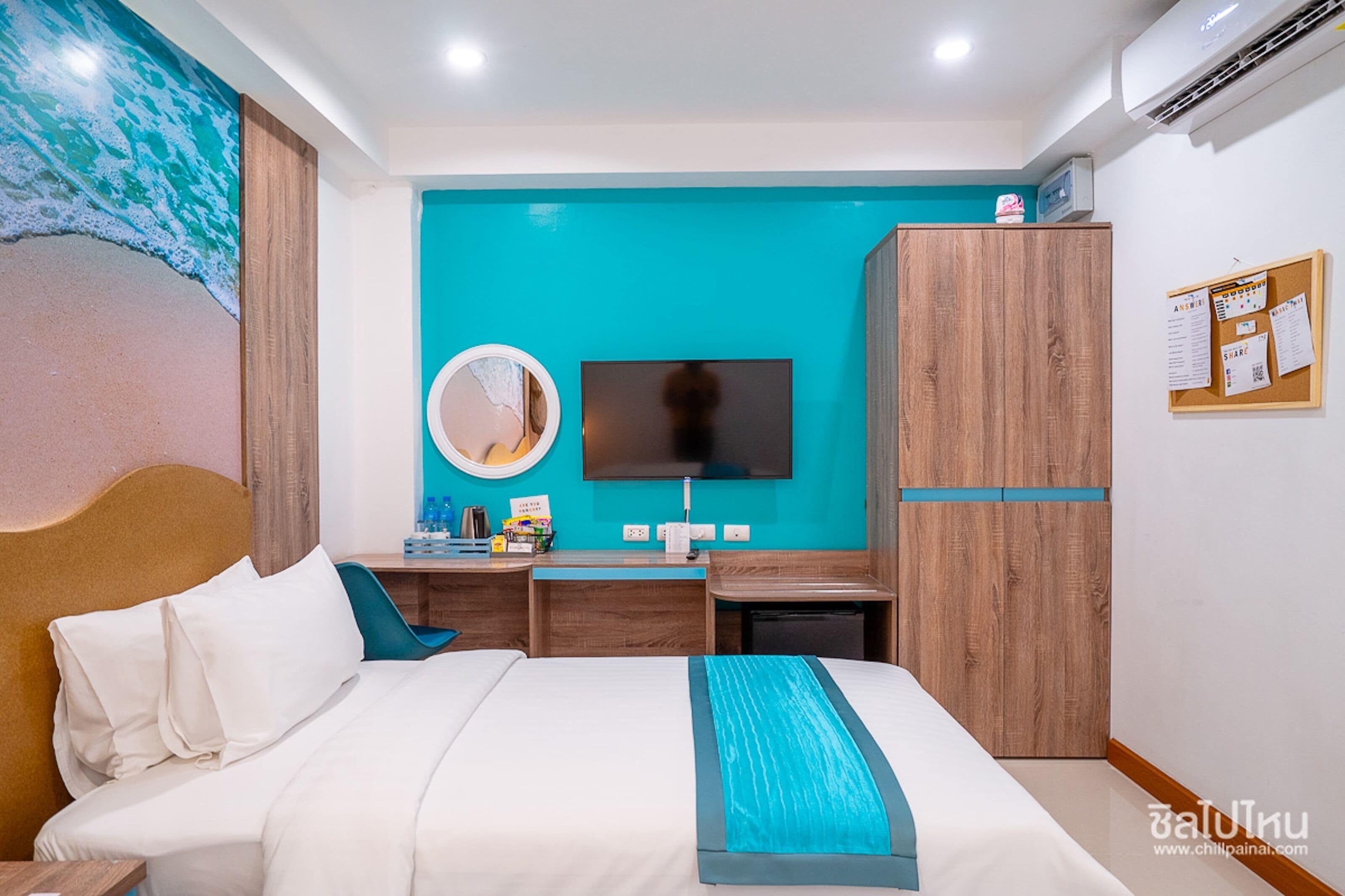 A hotel room with a bed, a desk, a TV, a mirror, and a bulletin board.