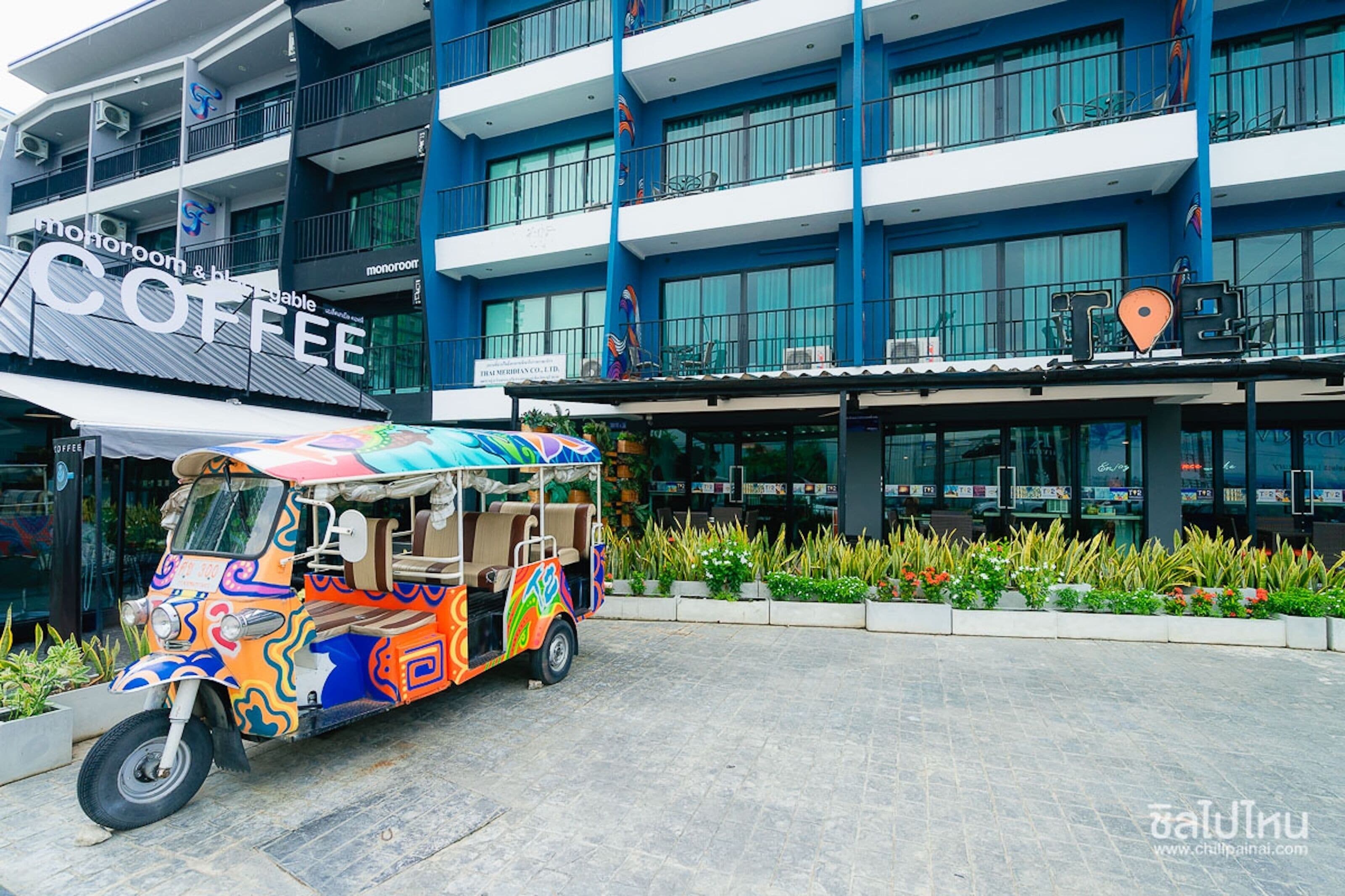 Un tuk-tuk colorido estacionado frente a un hotel con un letrero que dice 'Monoroom & Coffee'.