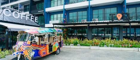 Un tuk-tuk colorido estacionado frente a un hotel con un letrero que dice 'Monoroom & Coffee'.