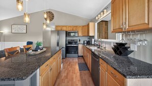 Eine moderne Küche mit Granit Arbeitsplatten, Holzschränken, Edelstahlgeräten und Pendelleuchten.