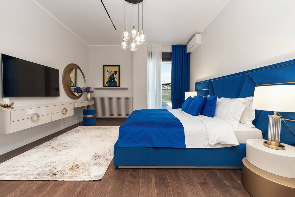 Un dormitorio moderno con cama, televisión, espejo y ventana con cortinas.