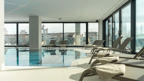 Ein Rooftop-Endlospool mit Liegestühlen und Blick auf die Stadt.