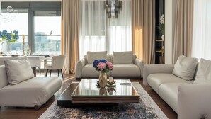 Ein modernes Wohnzimmer mit einem Glastisch, zwei Sofas, einem Esstisch und Blick auf die Stadt durch große Fenster.