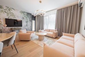 Una sala de estar moderna con un televisor de pantalla plana, sofás color beige, una mesa de centro redonda y piso de madera.