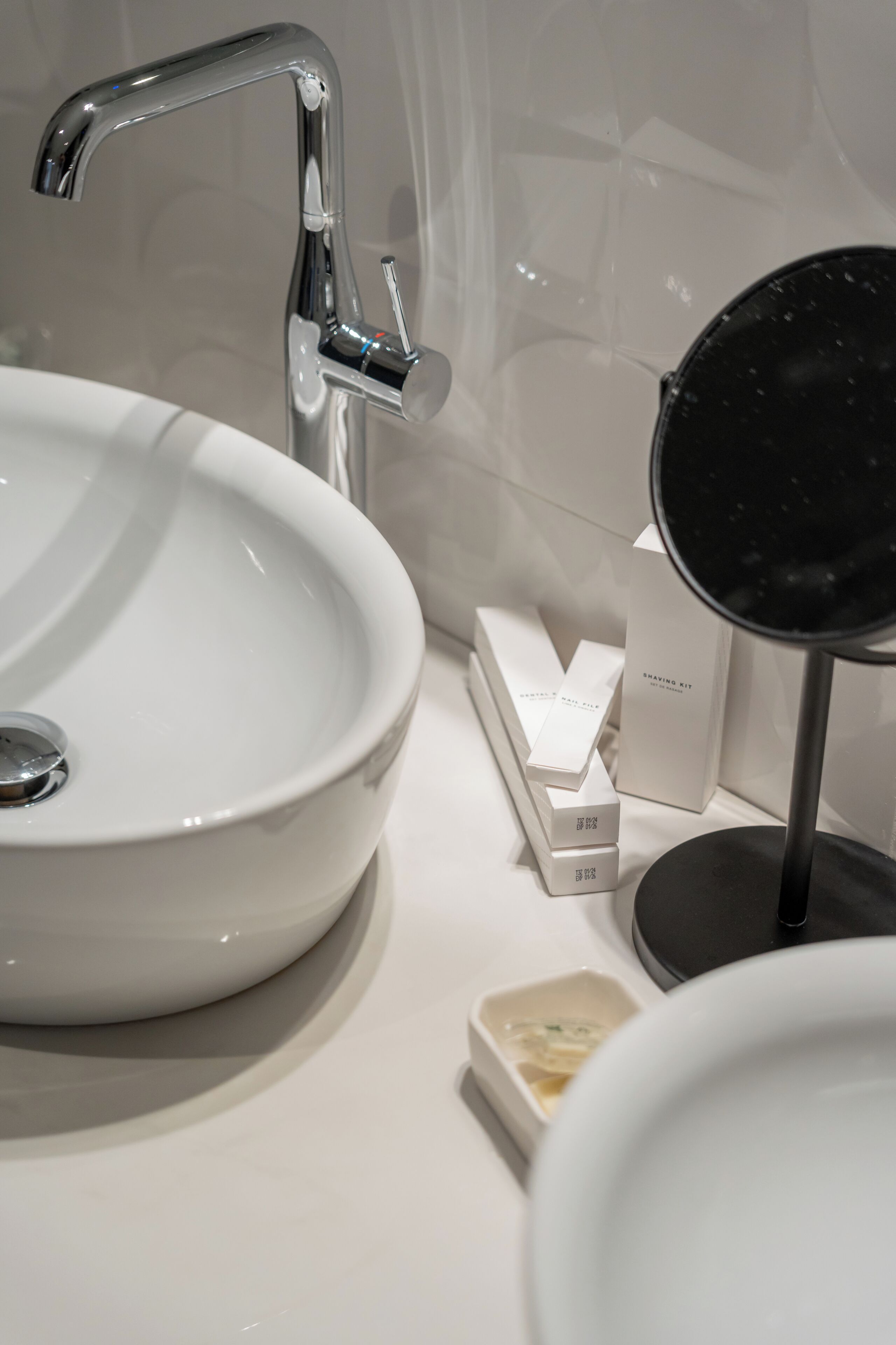 Un lavamanos de baño con una llave moderna, un espejo y un jabonera.