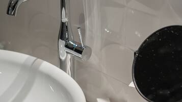 Un lavamanos de baño con una llave moderna, un espejo y un jabonera.