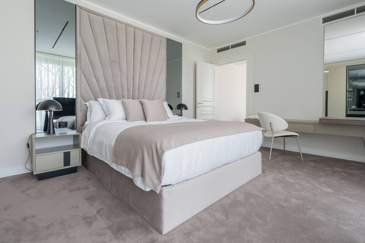 Un dormitorio moderno con una cama grande, mesitas de noche, una silla y un espejo.
