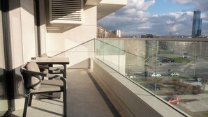A balcony with a chair and table, a view of a cityscape with buildings and a road. - New Belgrade Premium Hotel (Belgrade)