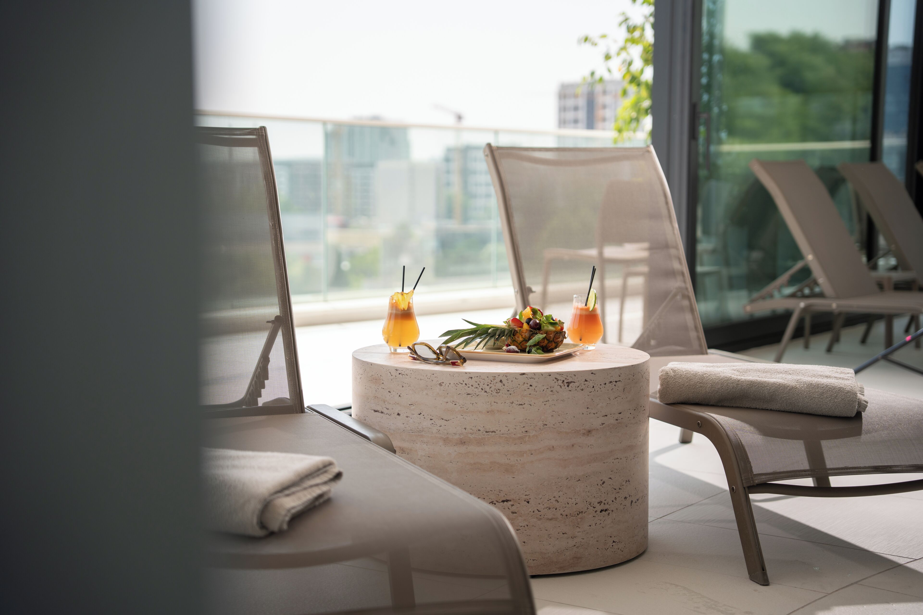 A modern lounge area with a round table, two chairs, and a view of the cityscape through large windows.