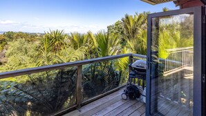 En balkon med udsigt over frodig, tropisk vegetation, en grill og en klapvogn.