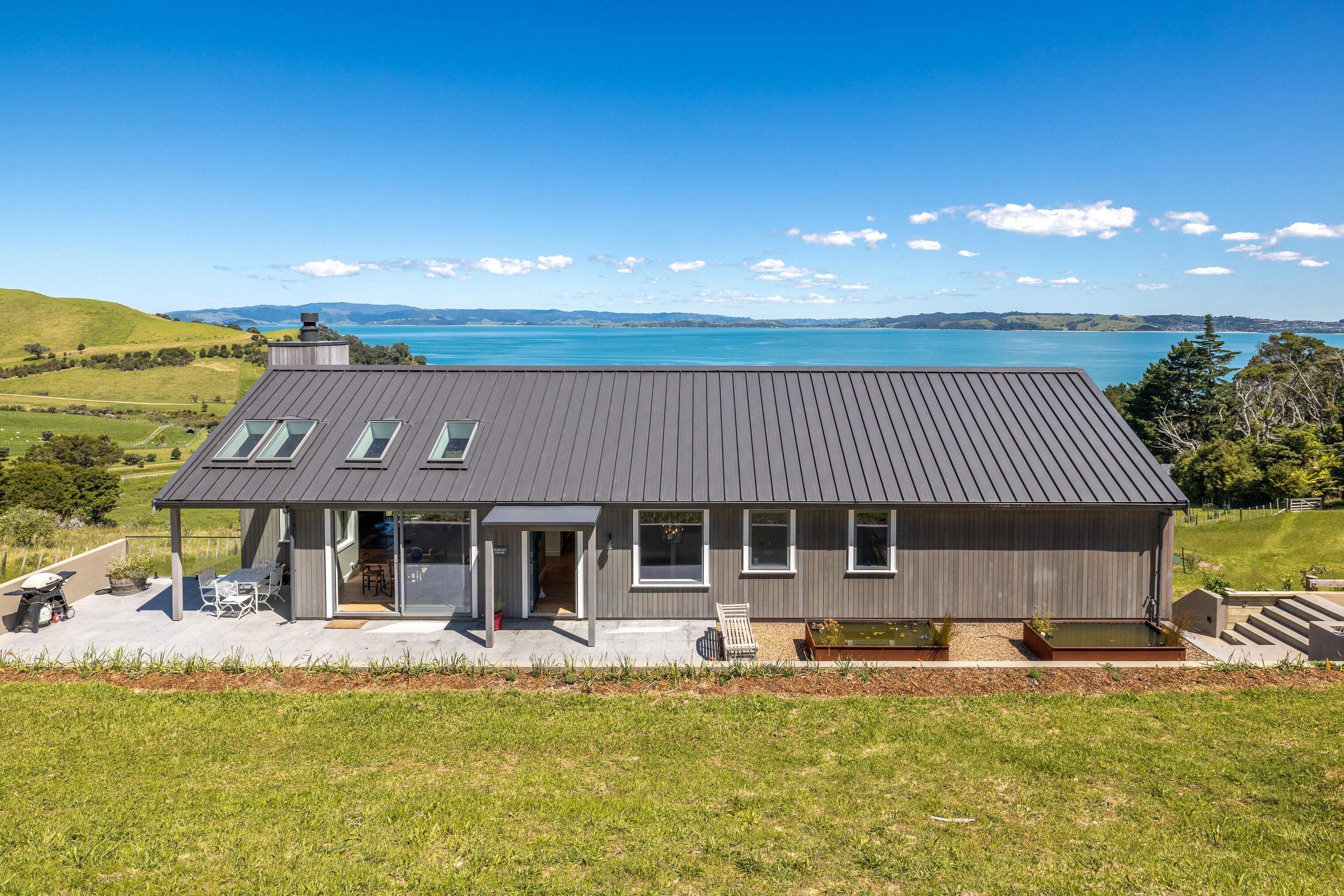 Une maison moderne avec un toit gris, de grandes fenêtres et une vue sur un lac.
