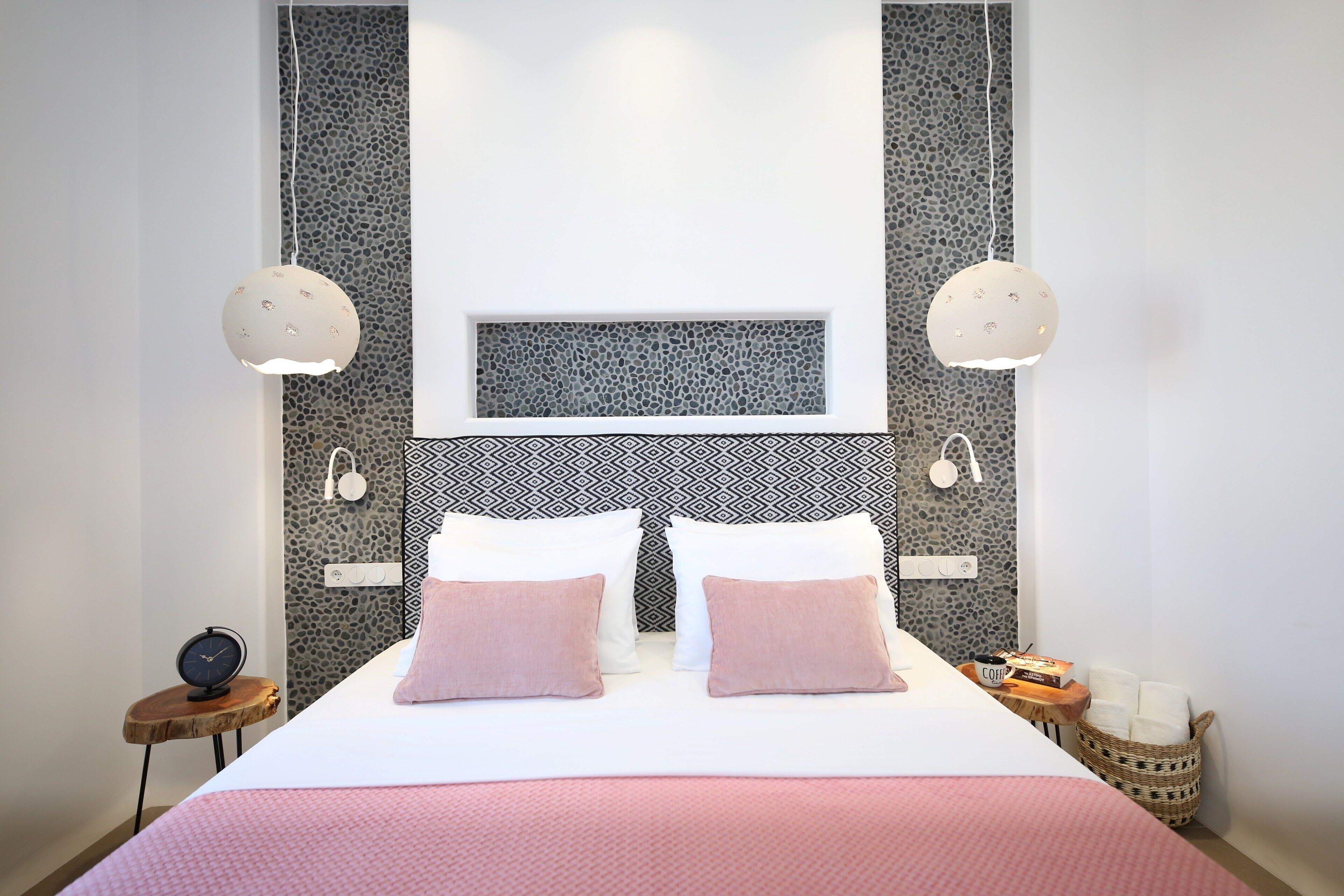 A neatly arranged bedroom with a bed, pillows, bedside tables, and a wall-mounted artwork.