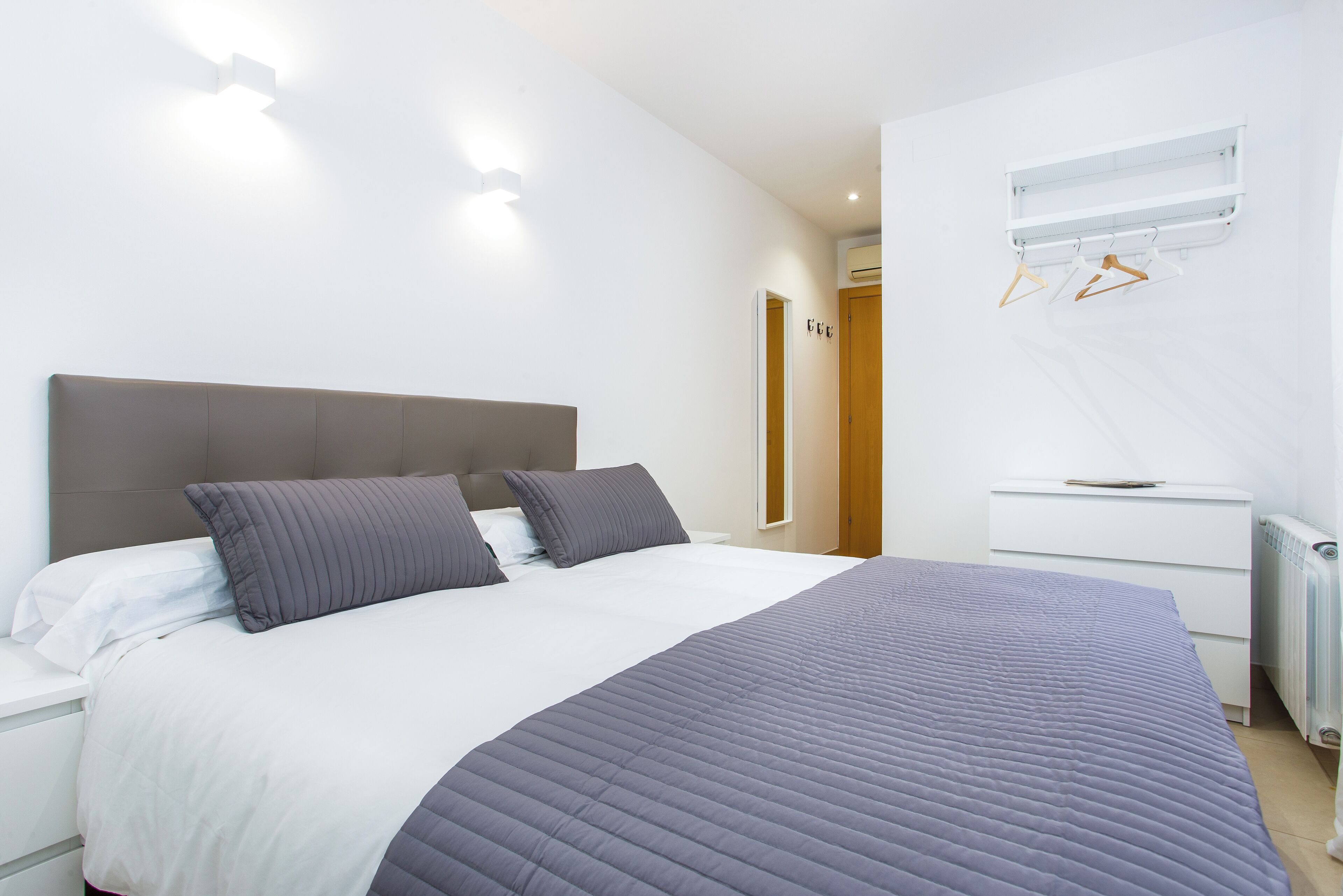 Un dormitorio moderno con una cama grande, una mesita de noche, un armario y un aire acondicionado instalado en la pared.
