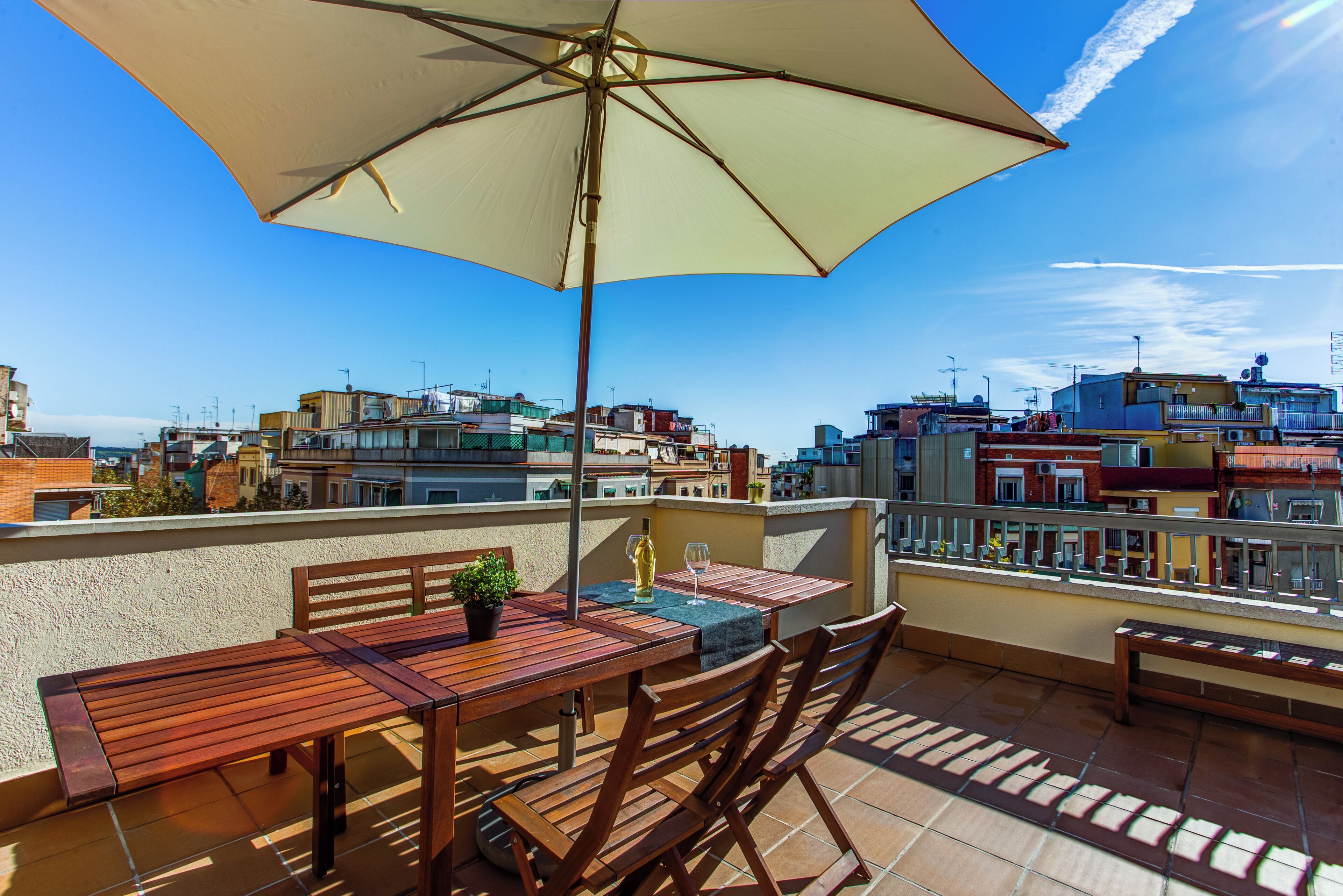 Una terraza en la azotea con una mesa de madera, sillas y un paraguas grande.