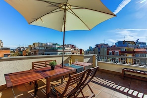 Una terraza en la azotea con una mesa de madera, sillas y un paraguas grande.