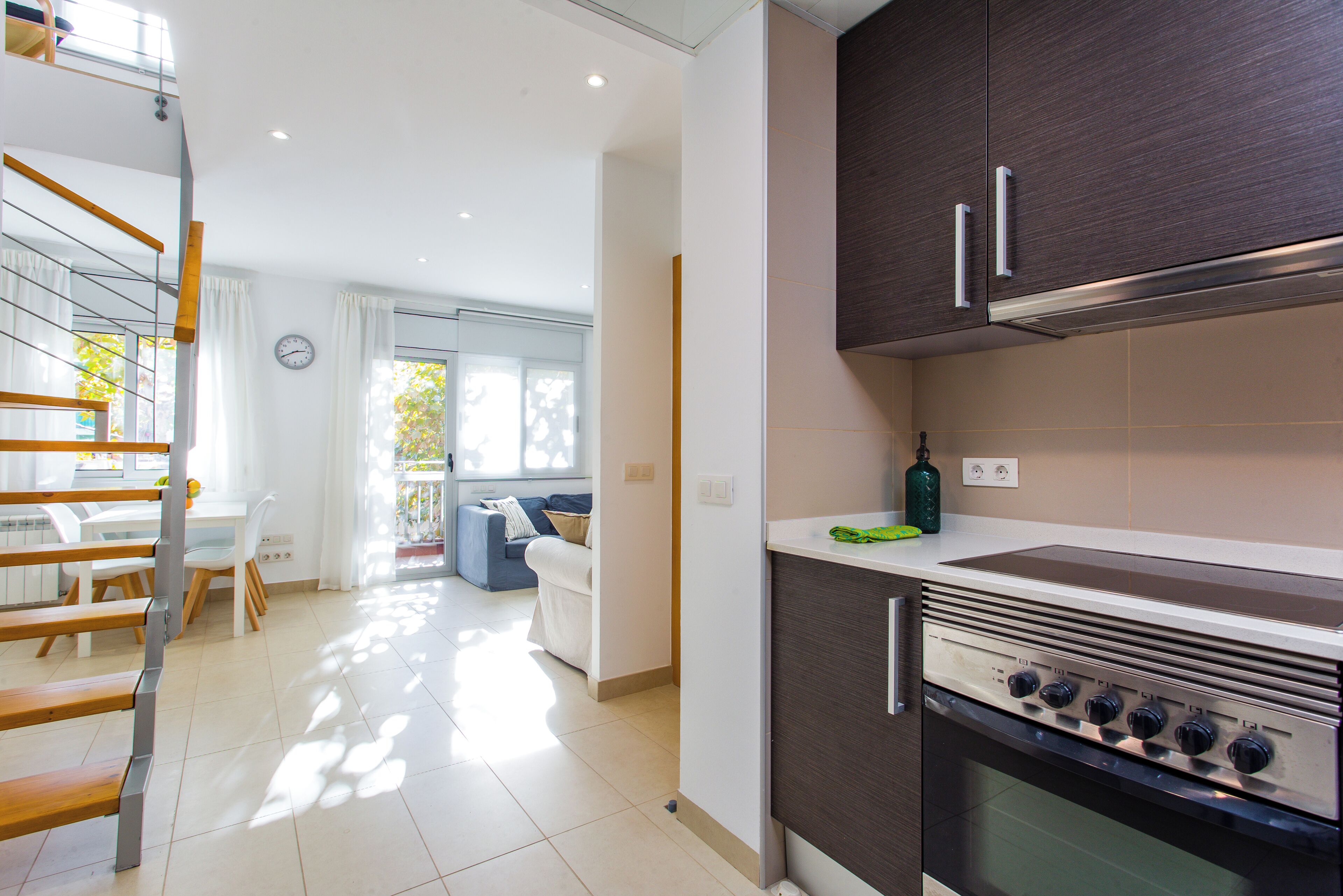 A modern kitchen with dark cabinets, a built-in oven, and a dining area with a white table and chairs.