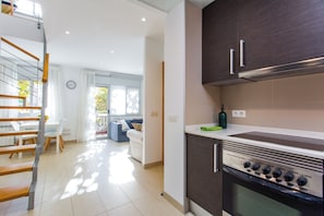 Una cocina moderna con armarios oscuros, horno empotrado y comedor con mesa y sillas blancas.