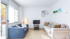 A modern living room with a blue sofa, a beige sofa, a TV on a stand, and a shelf with bottles. - Feriapiso Apartments Palmer (L'Hospitalet de Llobregat)