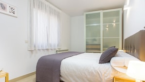 A neatly arranged bedroom with a bed, a bedside table, a lamp, and a window with sheer curtains. - Feriapiso Apartments Palmer (L'Hospitalet de Llobregat)