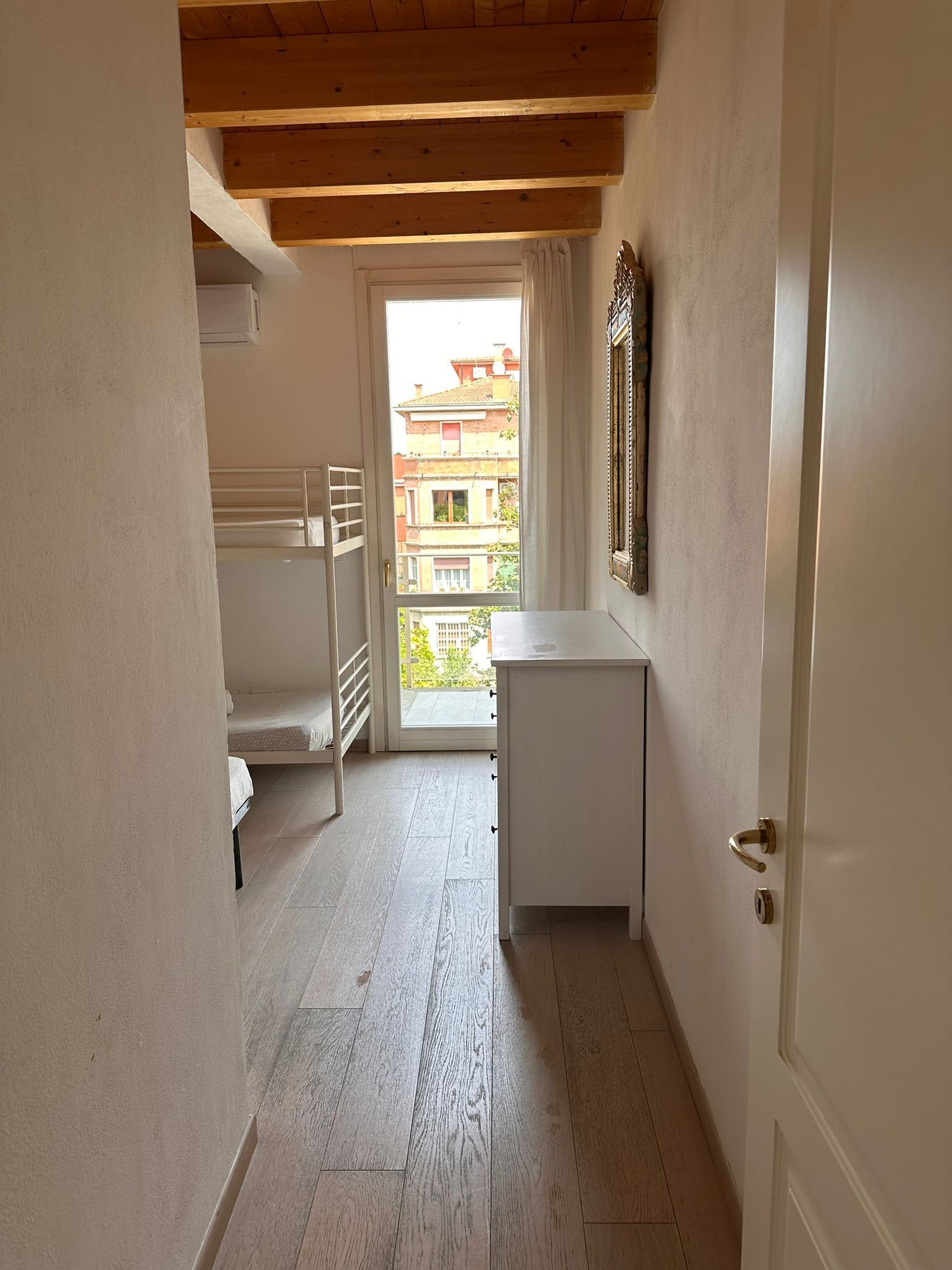 Un couloir étroit avec un plafond en bois, une porte blanche et une fenêtre donnant sur un balcon.