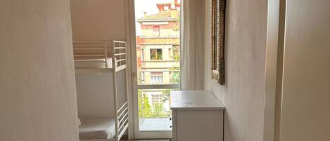 Un couloir étroit avec un plafond en bois, une porte blanche et une fenêtre donnant sur un balcon.