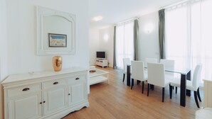 Una habitación amplia con una mesa de comedor blanca y sillas, un televisor y un mueble con cajones.