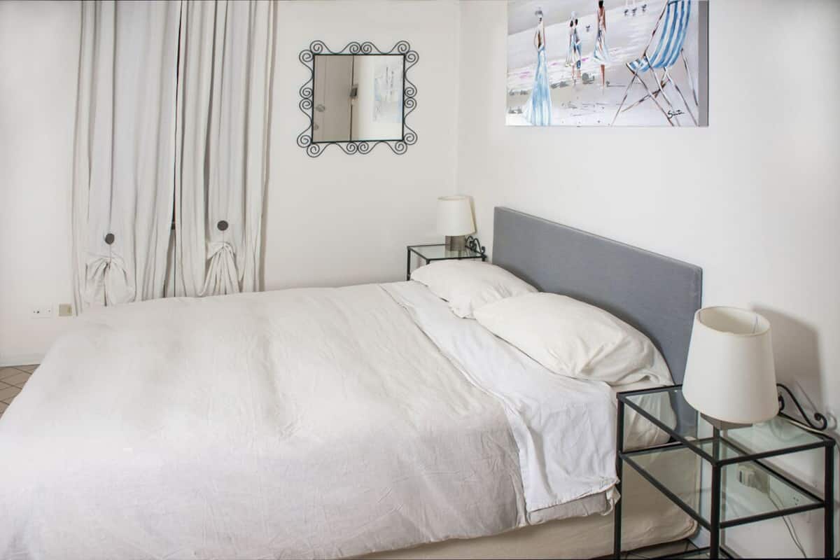 A neatly made bed with white linens, a grey headboard, and two bedside tables with lamps.