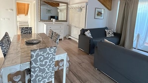 Un salón espacioso con techo de madera, una mesa de comedor con sillas estampadas, un sofá gris y un espejo grande.