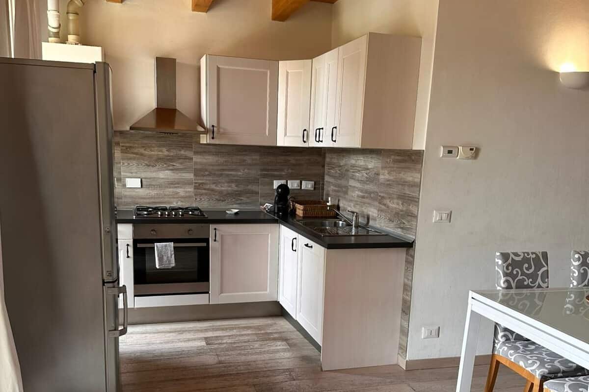 A modern kitchen with wooden beams, a stainless steel refrigerator, and a dining area with a patterned table and chairs.