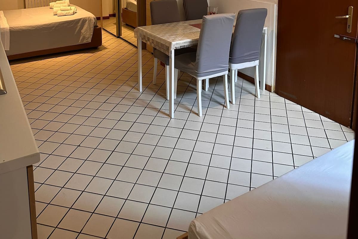 A hotel room with a bed, a table with chairs, a mirror, a door, and a ceiling light fixture.
