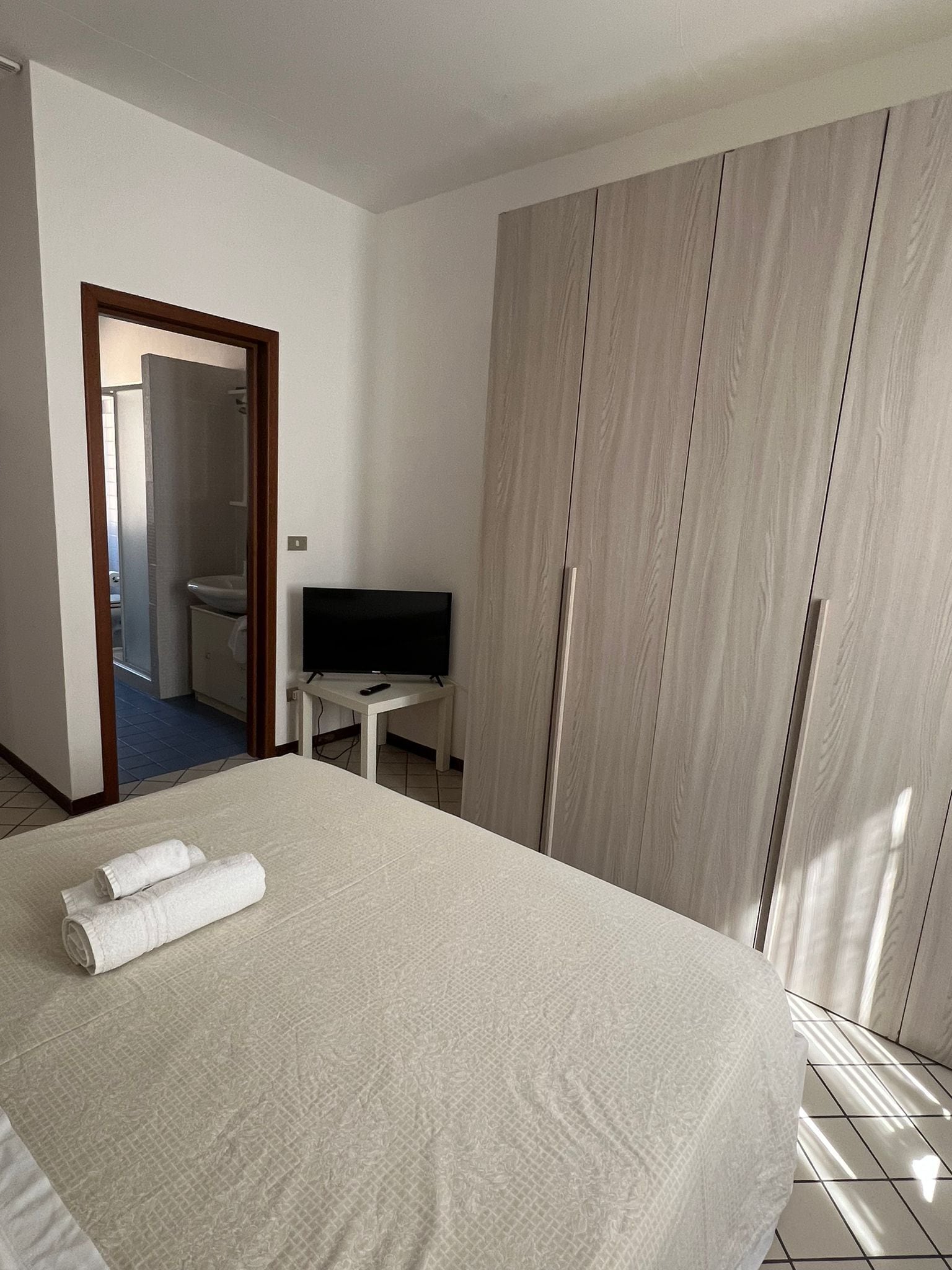 A hotel room with a bed, a TV, a wardrobe, and a bathroom visible through an open door.