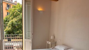 Un dormitorio con cama, mesita de noche, lámpara y vistas al balcón exterior.