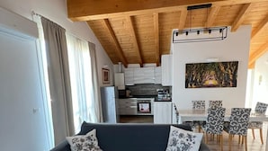 Una sala de estar moderna con un sofá oscuro, techo de madera y un comedor al fondo.