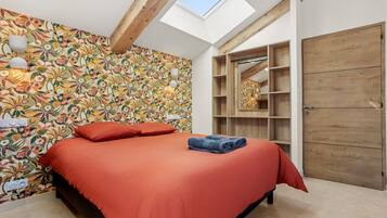 Une chambre dotée d’une lucarne, d’un lit avec une literie rouge, d’un mur à motifs et d’étagères en bois intégrées.