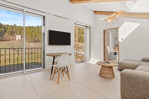 Un vaste espace de vie avec balcon, un téléviseur à écran plat, une table à manger avec des chaises, une petite table basse ronde et un canapé.